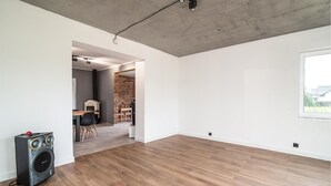 A spacious room with wooden flooring, a large window, and a brick wall.