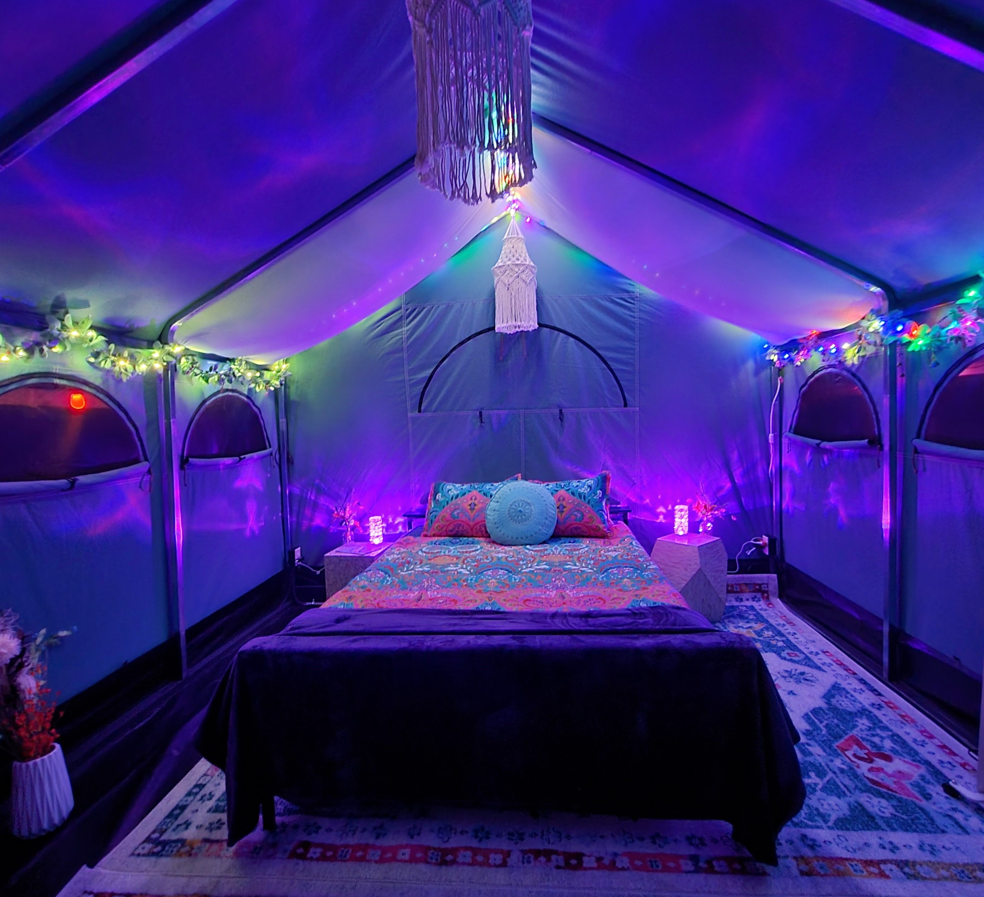 A tent with a bed, decorative lights, and a hanging macrame piece.