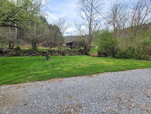 A gravel driveway leading to a green lawn with trees and a building in the background.