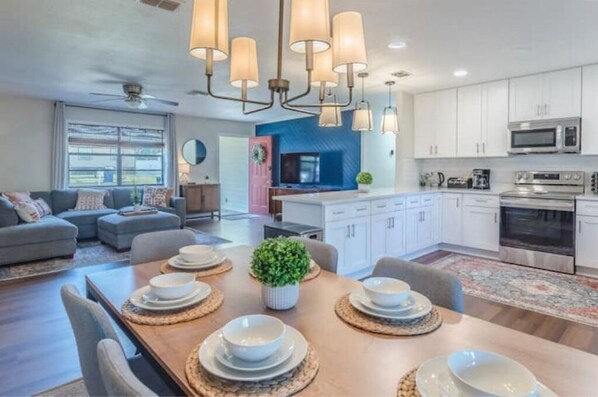 Enjoy meals at the dining table surrounded by comfortable chairs, with a fully equipped kitchen and a large window for natural light.