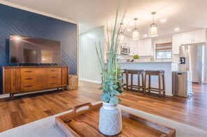 Relax in this stylish living room with a flat-screen TV, coffee table, and kitchen area featuring a refrigerator, microwave, and sink.