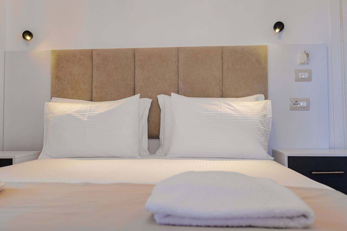 A neatly made bed with white linens and a folded towel on the side.
