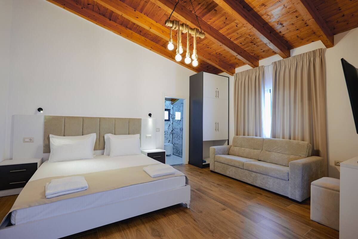 A modern bedroom with a large bed, a sofa, and a wooden ceiling.