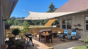 Een overdekt terras met een barbecuehoek, buitenmeubilair en een zonnescherm.