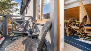 Un balcon avec des fauteuils et une table en osier, un intérieur en bois avec des meubles en rotin, et une vue sur l’extérieur.