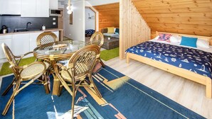 Une chambre d’hôtel compacte avec un lit en bois, une petite kitchenette, un coin repas avec des chaises en osier et un escalier menant à un niveau supérieur.