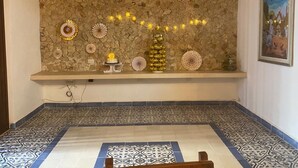 Una habitación con pared de piedra, pisos de baldosas decorativas, un estante con adornos y un cuadro enmarcado.
