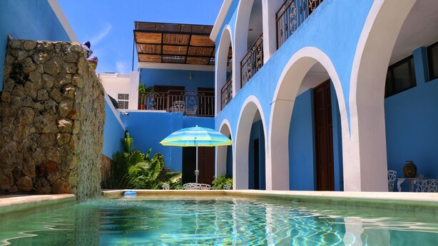 Un área de piscina con agua cristalina, muros de piedra y arquitectura azul y blanca.