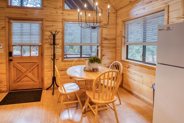 L’intérieur d’un chalet en bois comprend une table à manger, des chaises, un lustre et un réfrigérateur.