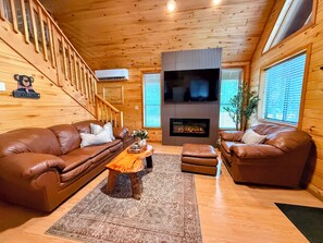 A cozy living room with a fireplace, leather sofas, and a wooden staircase. - Cabin w/ Loft, Private hot tub + Stargazing deck! (Overgaard)