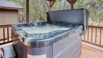 A hot tub on a wooden deck with a wooden structure overhead, surrounded by trees.