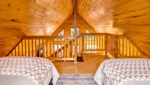 Um quarto de sótão acolhedor, com vigas de madeira, uma escada e duas camas com roupa de cama estampada.