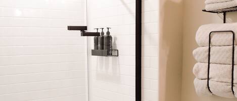 Een moderne badkamer met een glazen douchecabine, een wit toilet en een handdoekrek met opgevouwen handdoeken.