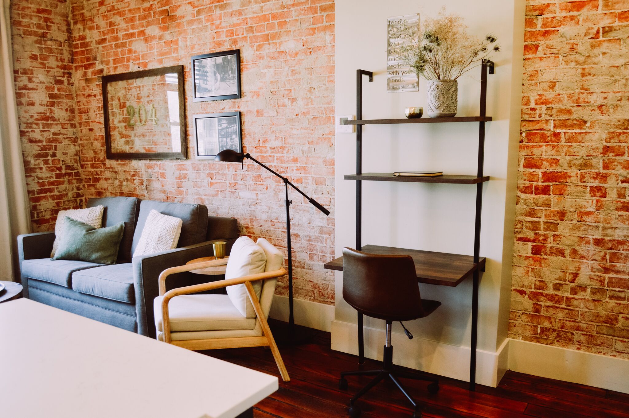 Une pièce avec un mur en briques, un canapé, une chaise, un bureau et une bibliothèque.
