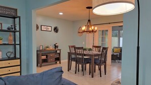 Uma área de refeições com mesa e cadeiras de madeira, um espaço para café e uma estante com objetos decorativos.