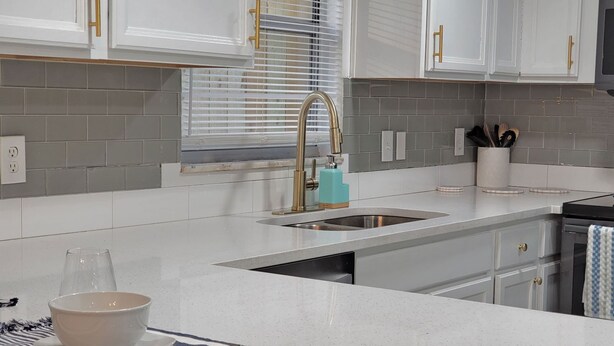 Cozinha moderna com painel de azulejos cinza, armários brancos e uma pia de aço inoxidável.