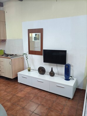 A kitchen with a gas stove, a white cabinet, a flat-screen TV, and a blue fan. - Iter Away Dunes (La Oliva)
