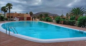 A swimming pool with a tiled deck, surrounded by palm trees and a mountain in the background. - Iter Away Dunes (La Oliva)