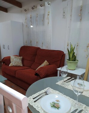 A cozy living room with a red sofa, a small table with a glass of water, a plate, and cutlery. There is a potted plant on a small table beside the sofa. - Iter Away Dunes (La Oliva)