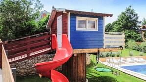 Une cabane en bois avec un toboggan rouge, un mur en pierre et un espace piscine.