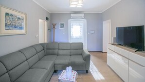Un salon avec un canapé d’angle gris, un téléviseur à écran plat posé sur un meuble en bois et un tableau accroché au mur.