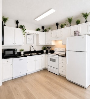 A modern kitchen with white cabinets, a black countertop, a white refrigerator, and a stove.