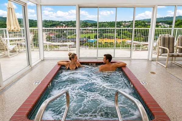 Un jacuzzi con dos personas, rodeado por un recinto de vidrio que ofrece vista a una zona residencial.