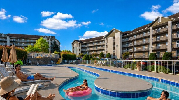 Zona de piscina con sillones de playa y sombrillas, rodeada de edificios de varios pisos.