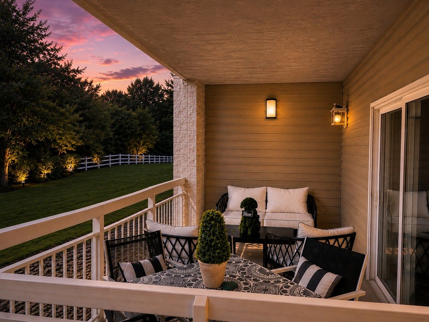 A covered outdoor seating area with a sofa and chairs, a small table, and a potted plant.