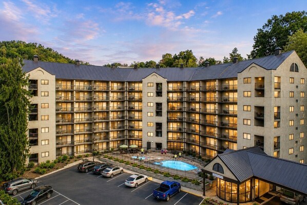 A multi-story hotel with a pool, parking lot, and a covered area.