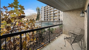 Un balcon donnant sur un immeuble, avec une clôture en métal et une chaise.
