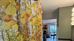 A hallway with a large autumn leaf wall, a dining area in the background, and a kitchen area with a modern design.