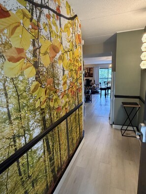 A hallway with a large autumn leaf wall, a dining area in the background, and a kitchen area with a modern design.