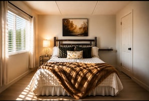 A bedroom with a bed, a bedside lamp, a painting on the wall, and a window with blinds.