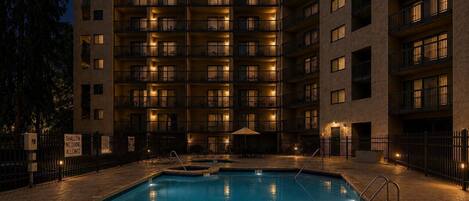 A multi-story hotel with a swimming pool, outdoor lighting, and a sign indicating shallow water.