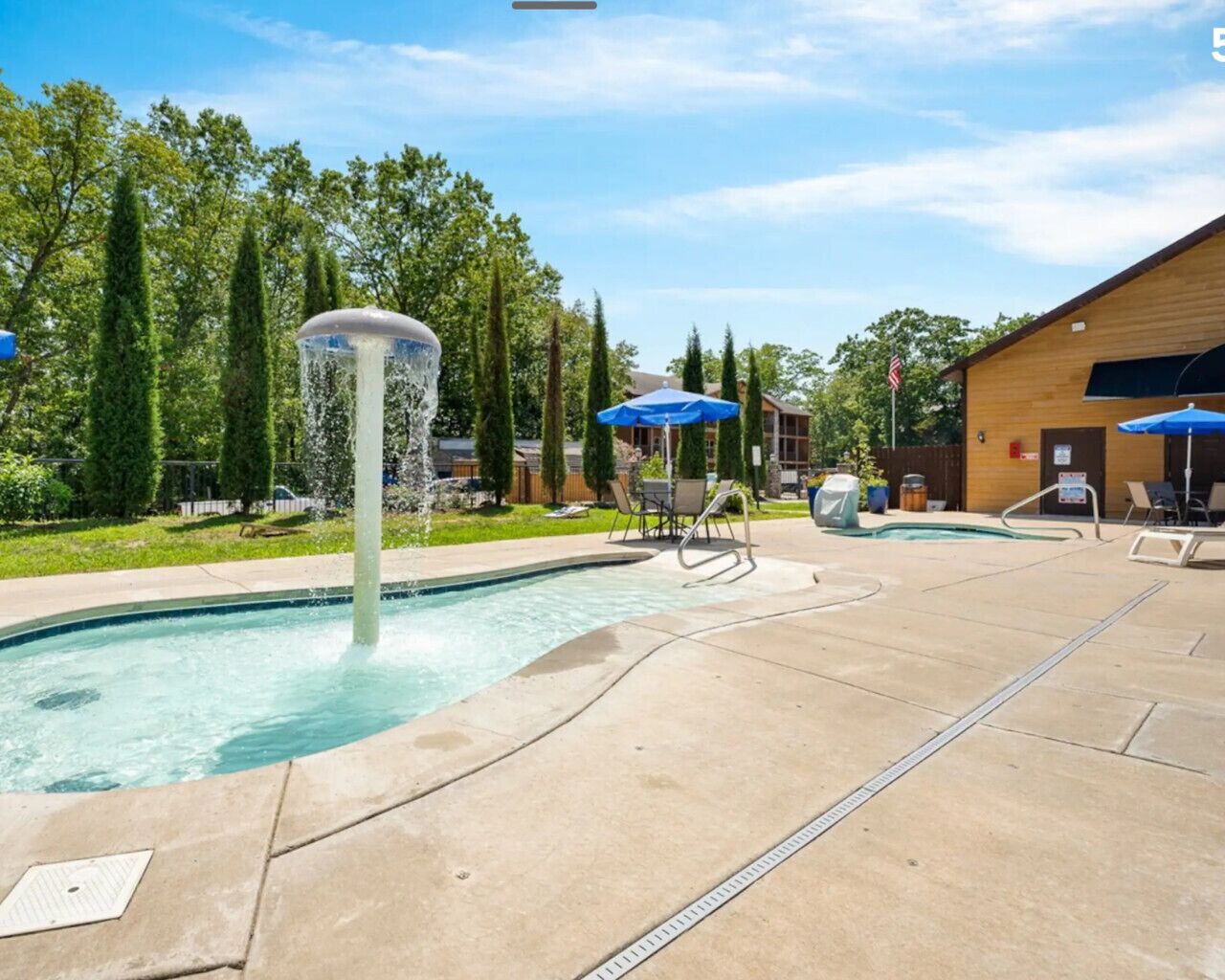 A swimming pool with a water fountain, lounge chairs, and umbrellas.