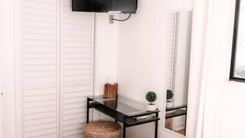 A bedroom with a bed, a desk with a flat-screen TV, a ceiling fan, and a white wardrobe.