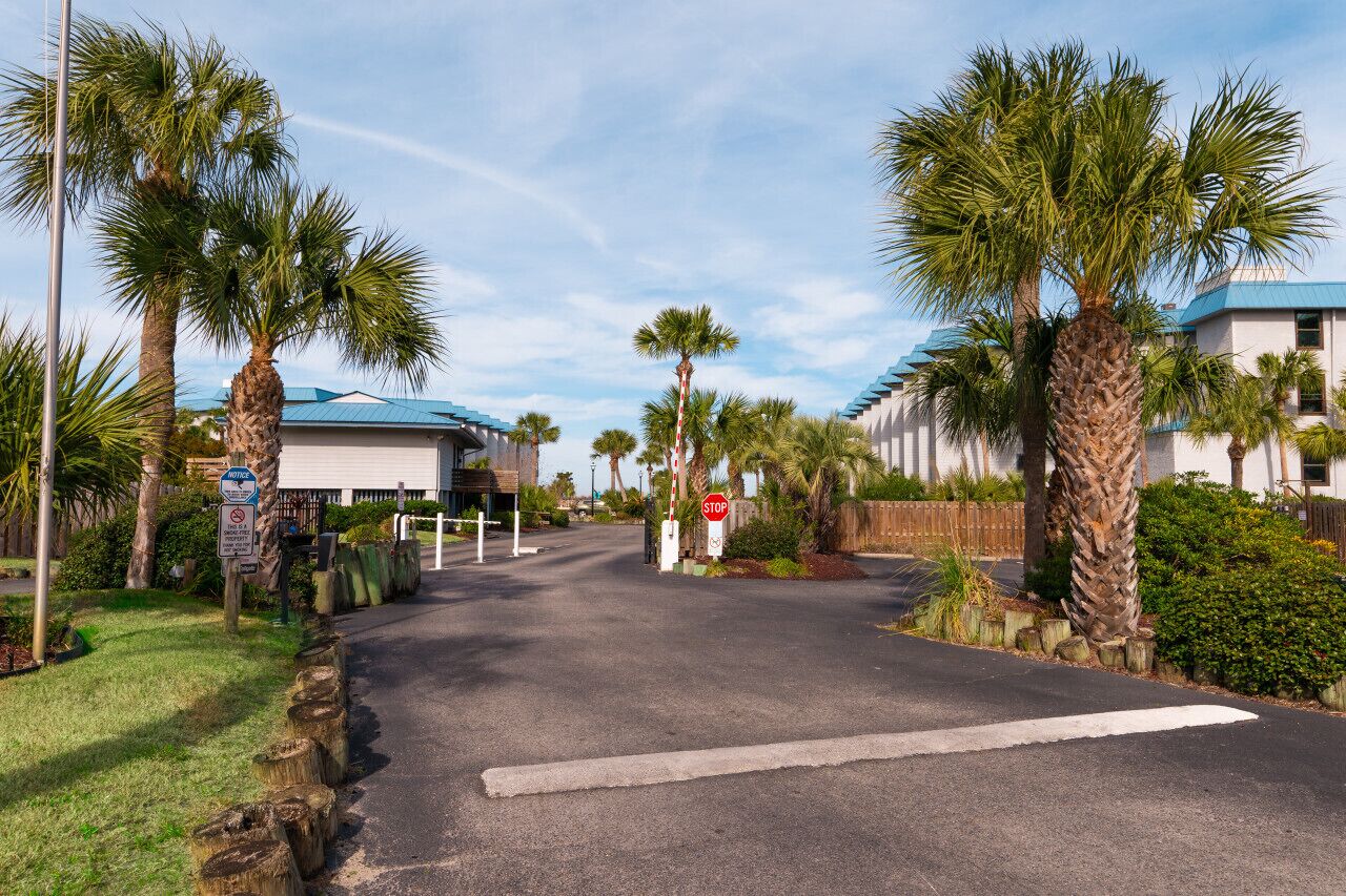 A gated entrance with palm trees and a stop sign.