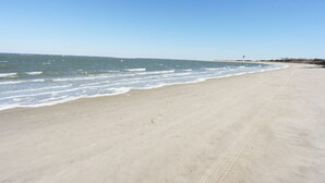 Une plage de sable fin aux vagues douces, un ciel dégagé et une côte lointaine.