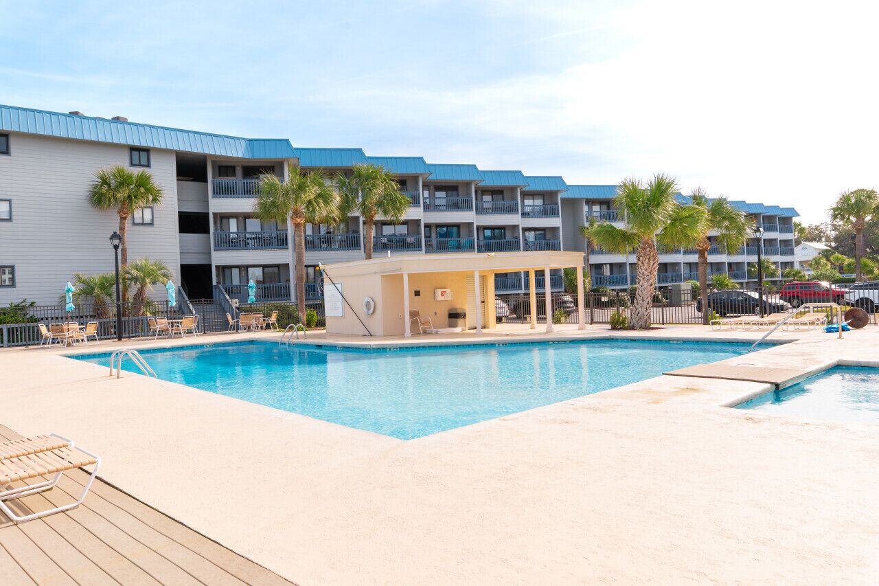 A hotel with a swimming pool, outdoor seating, and palm trees.