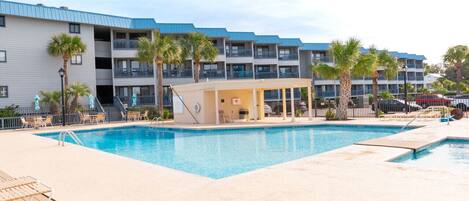 A hotel with a swimming pool, outdoor seating, and palm trees.
