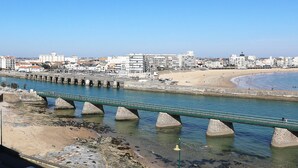 Eine Küstenstadt mit einer markanten Brücke über einem Fluss, einem Sandstrand und einem klaren, blauen Himmel.