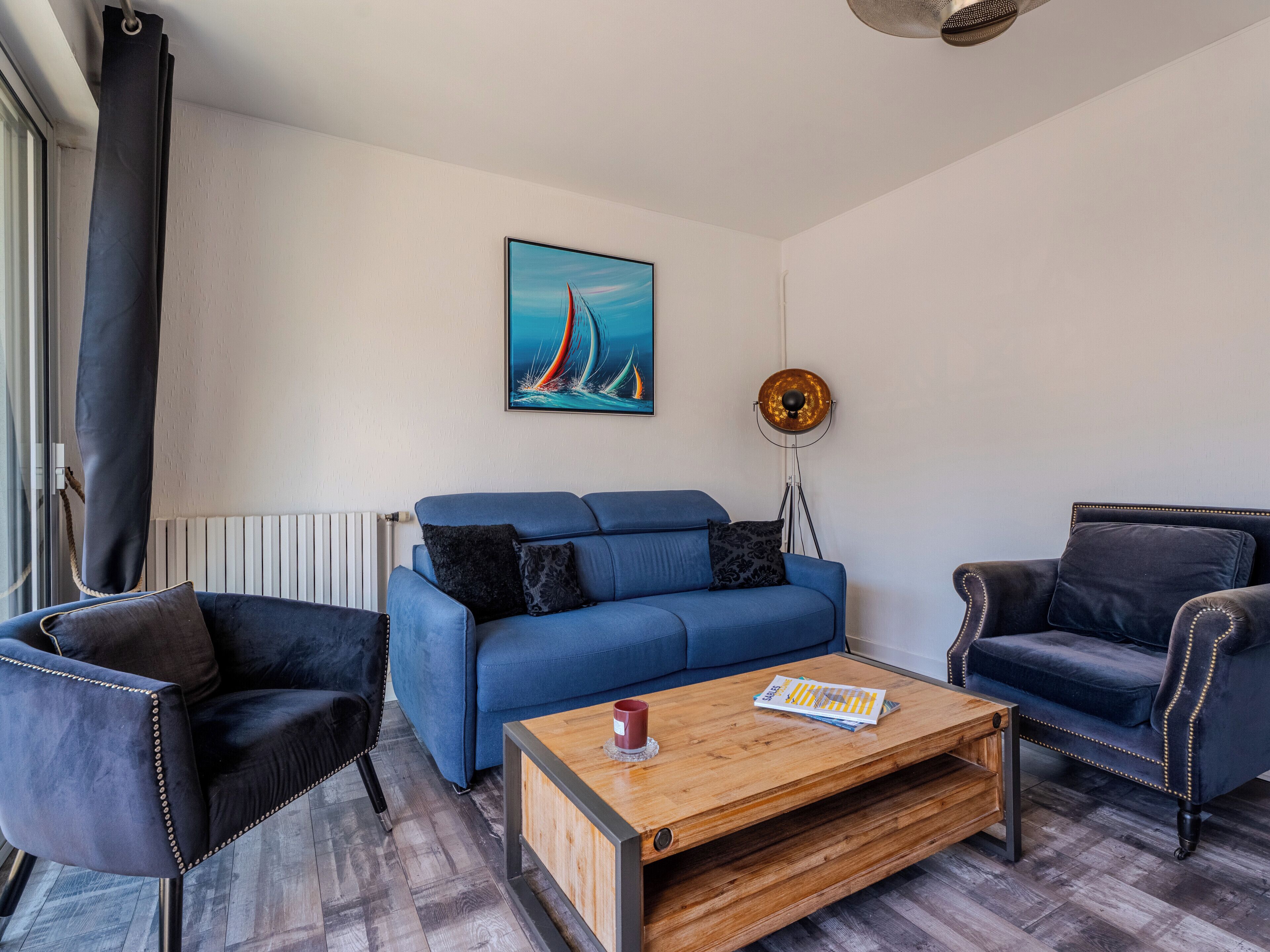 Una sala de estar con un sofá azul, dos sillones negros, una mesa de centro de madera y una lámpara de pie.