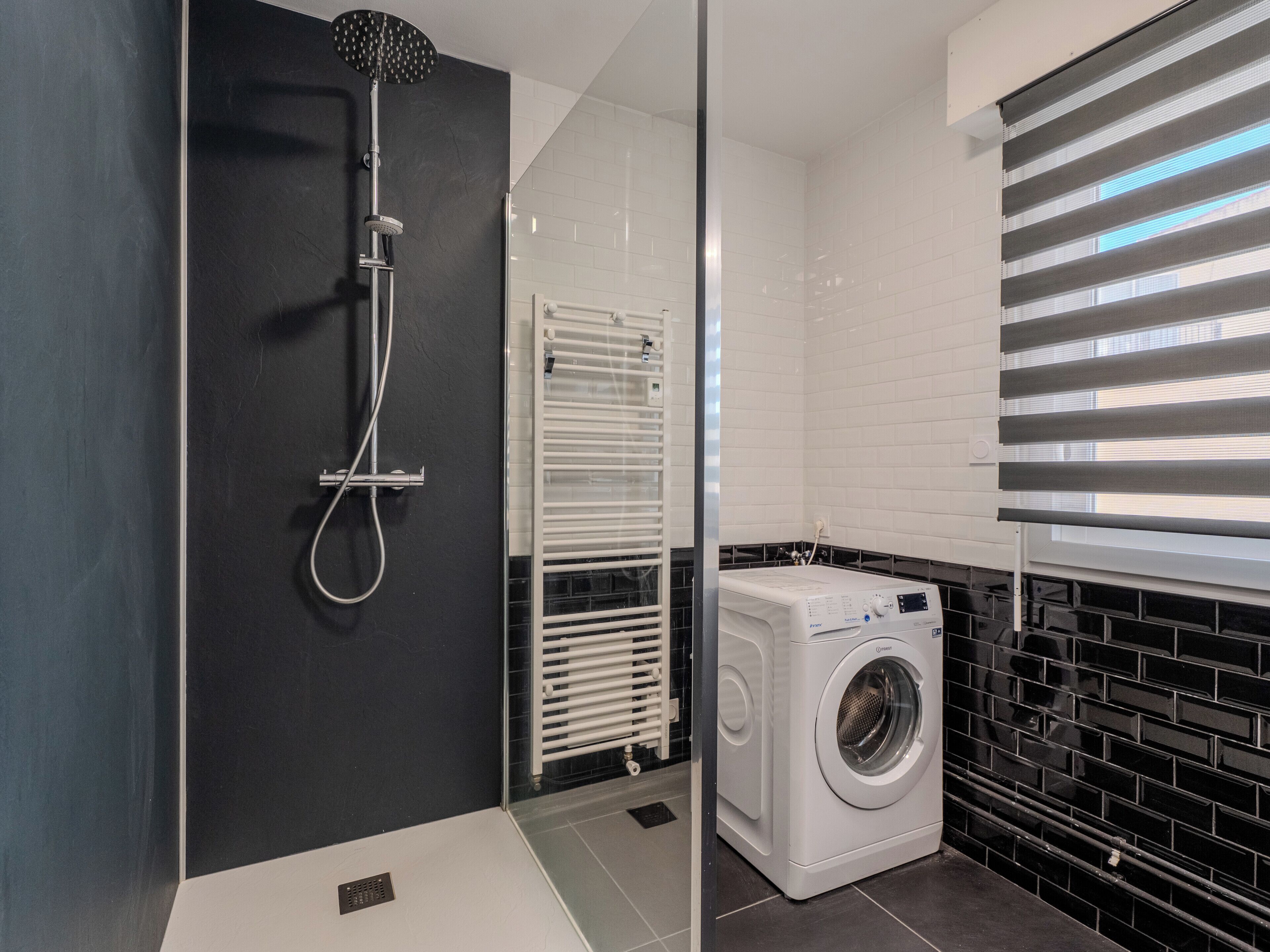 A modern bathroom with a glass-enclosed shower, a built-in washing machine, and a radiator.