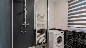 A modern bathroom with a glass-enclosed shower, a built-in washing machine, and a radiator.