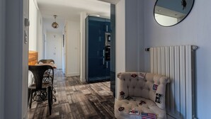 Una habitación con piso de madera, un sillón capitonado con parches, un espejo y un radiador.