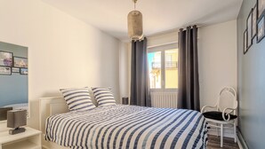 Un dormitorio con cama, mesita de noche, silla y una ventana con cortinas.