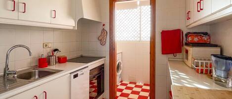 A compact kitchen with white cabinets, a red and white checkered floor, a sink, a stove, and a microwave.