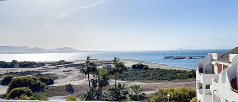 A balcony with a view of a beach, boats, and distant mountains.