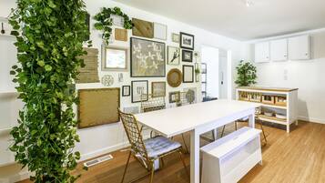 Un comedor con una mesa blanca, una silla con asiento acolchado y un banco. Hay una pared con varios cuadros enmarcados y una planta verde grande.